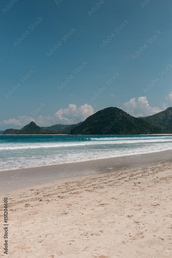 Landscape with a tropical beach with green hills, rocks on the background, water is azure and sand is white, Indonesia, Lombok Landscape with a tropical beach with green hills, rocks on the background, water is azure and sand is white, Indonesia, Lombok