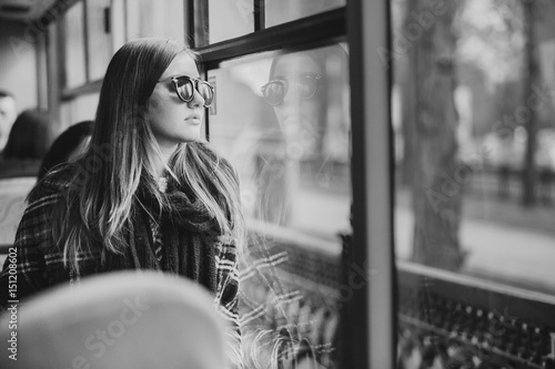Girl in sunglasses stands at the window of the bus and dreams