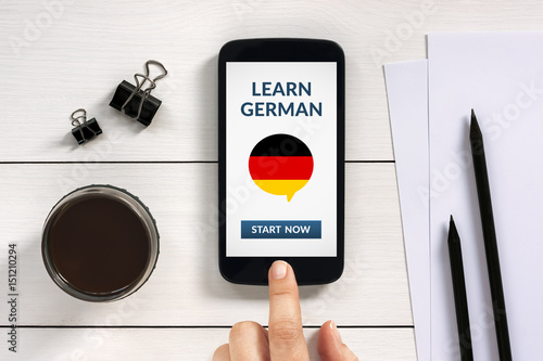 Learn german concept on smart phone screen with office objects on white wooden table. All screen content is designed by me. Flat lay