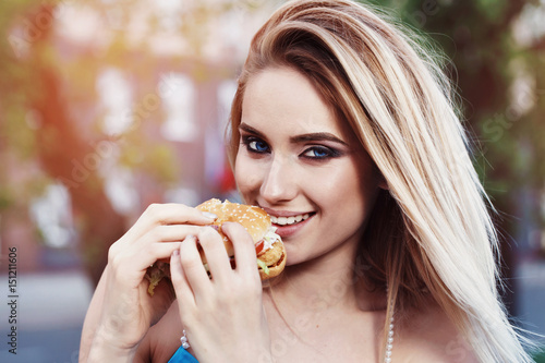 Beautiful blond girl eating a delicious hamburger outdoors on a spring sunny evening  closeup
