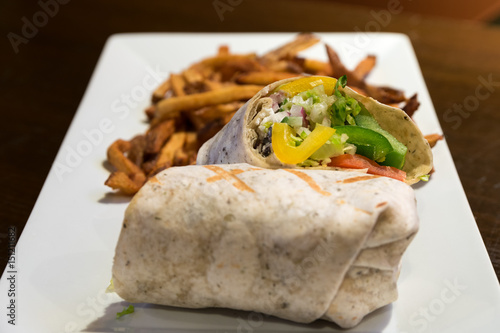 A Greek vegetarian wrap served with golden fries on a white plate.