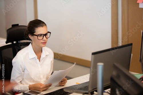 Businesswoman holding documets while looking at laptop photo