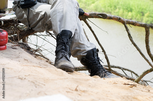 Traveler in leather boots sit over a cliff above the river near gas burner