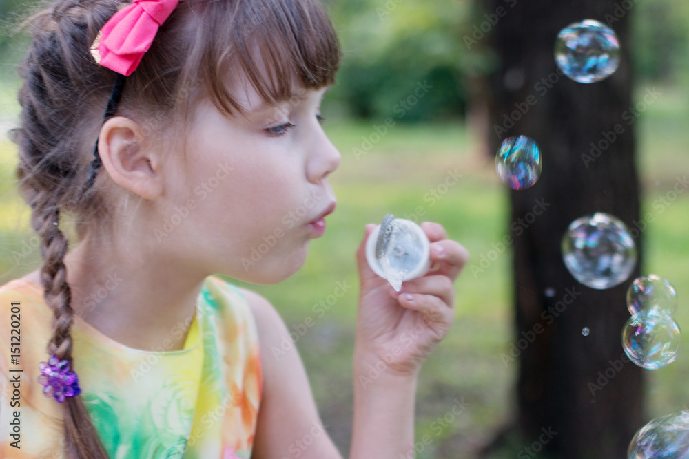 Little girl with cute pigtails and a sundress the color blow bubbles on a warm day