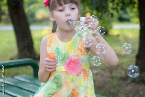 Beautiful little girl in color dress that takes lots of soap bubbles warm day, focus on bubbles