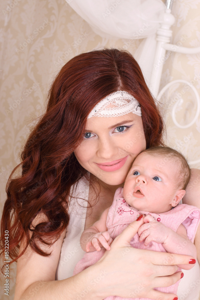 Happy young mother in a white silk dress, holds her baby in her arms and smiling Happy young mother in a white silk dress, holds her baby in her arms and smiling