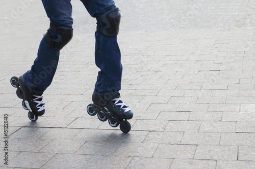 Young man in blue jeans roller-skates in the city with protective knee pads