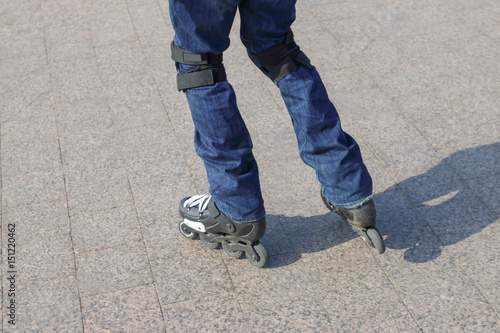 Young man in blue jeans roller-skates in the city with protective knee pads