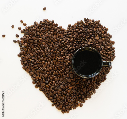 Coffee beans in the shape of heart and a cup of black coffee on a white background