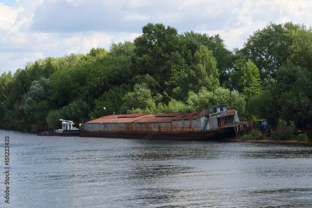 River watrer, lonely rusty cargo ship dire straits among bushes on summer day River watrer, lonely rusty cargo ship dire straits among bushes on summer day