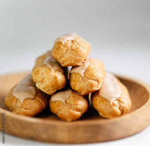 Eclairs on white background on wooden plate © Nataliia