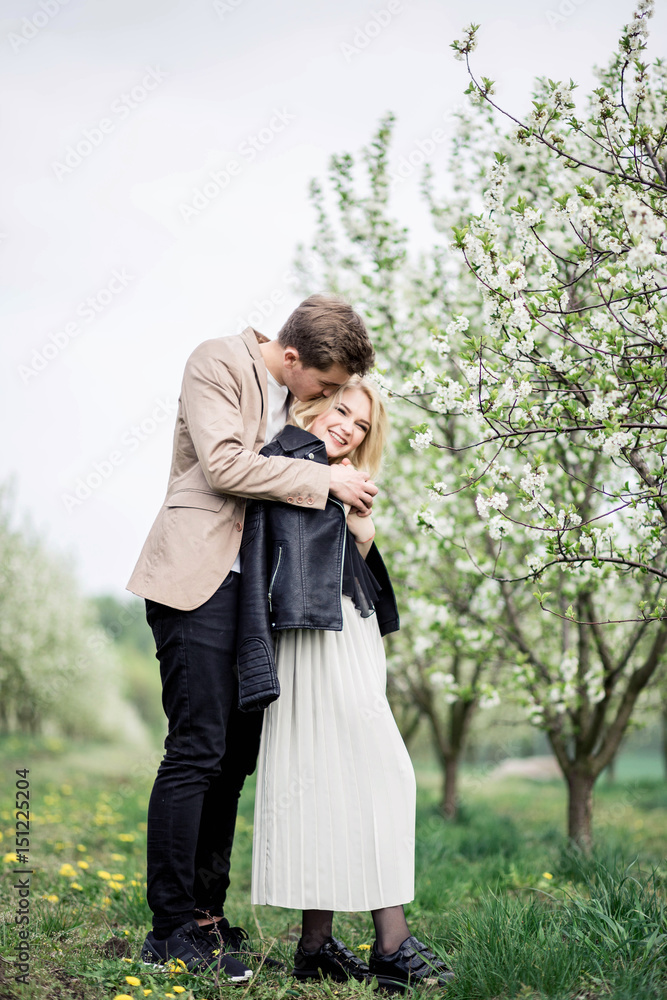 Handsome man standing behind his girlfriend in park and embracing her