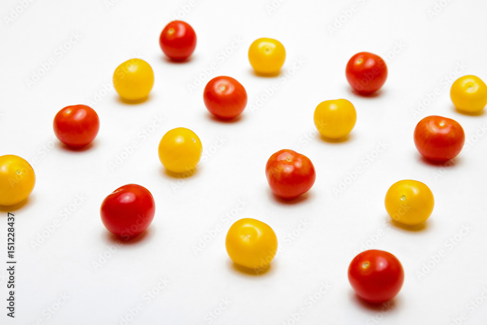 Red and yellow cherry tomatoes on a white background, in perspective view. Shallow depth of field. Red and yellow cherry tomatoes on a white background, in perspective view. Shallow depth of field.