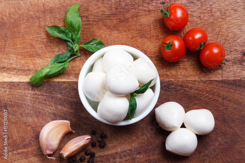 Cherry mozzarella in bowl  cherry tomatoes fresh basil  garlic and pepper on wooden board   up view