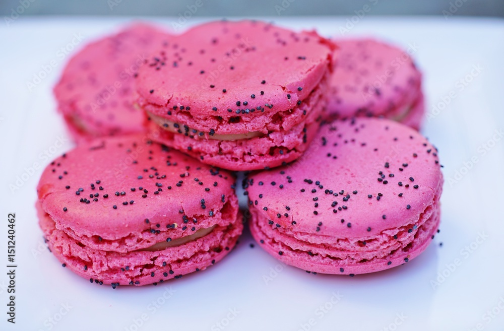 Pink strawberry and poppy seed macaron cookies on a white platter Pink strawberry and poppy seed macaron cookies on a white platter