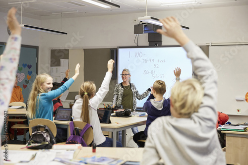 Teacher looking at students with hands raised in classroom photo