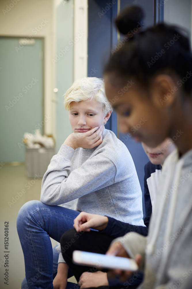 Bored middle school boy sitting with friends in corridor Bored middle school boy sitting with friends in corridor