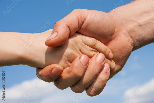Handshake of a child and an adult against a blue sky