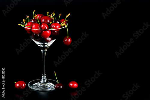 Kirschen im Cocktailglas vor schwarzem Hintergrund mit Textfreiraum