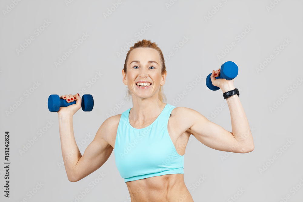 smiling middle-aged sports woman working out with dumbbells on the grey background smiling middle-aged sports woman working out with dumbbells on the grey background