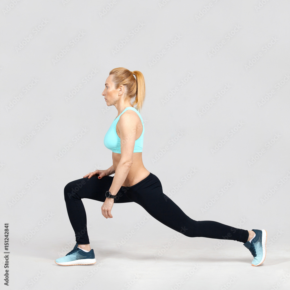 middle-aged sports woman doing lunge on the grey background middle-aged sports woman doing lunge on the grey background