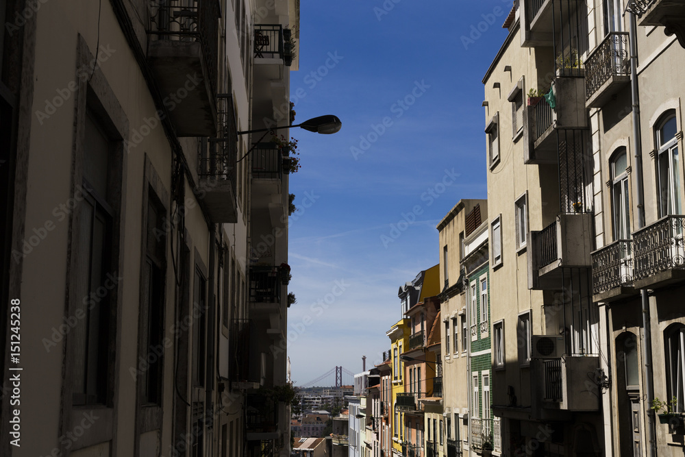 Streets of Lisbon, beautiful view with architecture and bridge on backgrounds. Portugal. Blue sky. Sunny weather.Typical tiles in buildings. Holidays and travelling.