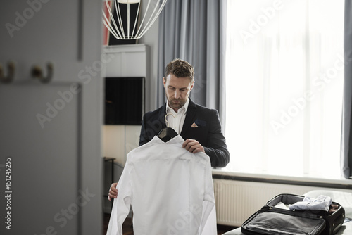 Businessman holding white shirt in coathanger against window at hotel room photo