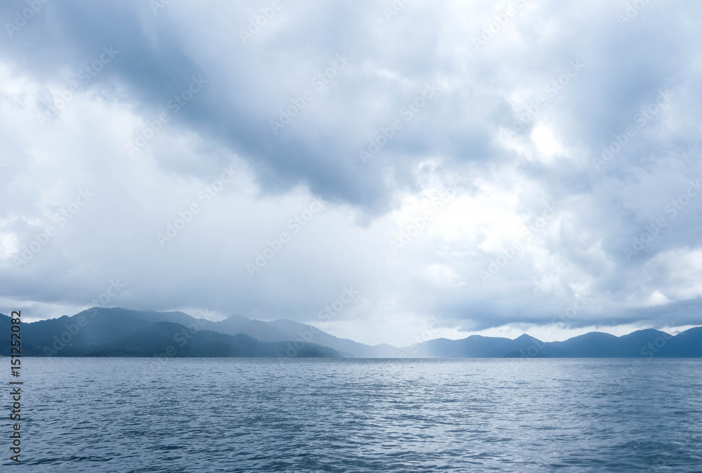 The blue ocean with some rain; mountains and cloudy sky as a background
