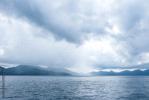 The blue ocean with some rain  mountains and cloudy sky as a background
