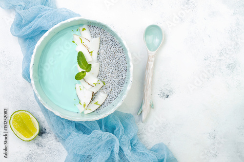 Vegan blue spirulina smoothie and chia pudding bowl topped with coconut flakes and lime zest. Overhead, flat lay, top view, copy space photo