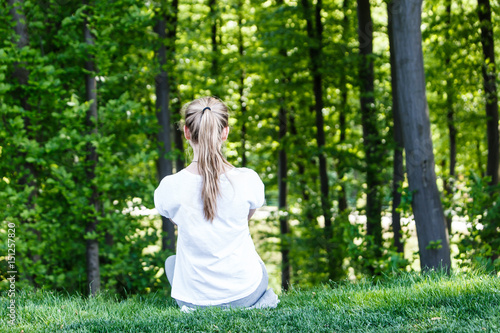 A girl in a white t-shirt sits and stares into the forest. Rear view.