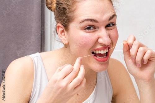 Canvas Print frowning beautiful young woman holding dental floss to clean teeth