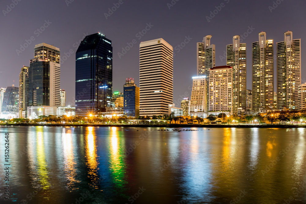 Benjakitti public park in Bangkok city in the twilight with skyscrapers and lights reflecting in the lake.