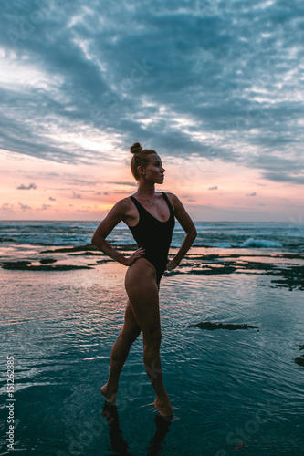 Attractive red hair woman stands on the beach in a black swimsuit during sunset, Indonesia, Bali