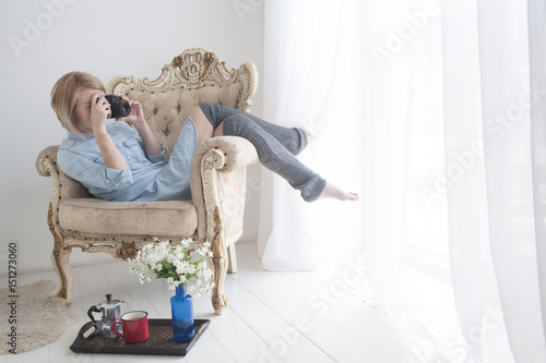 Beautiful young woman with photo camera in big comfortable chair near window photo