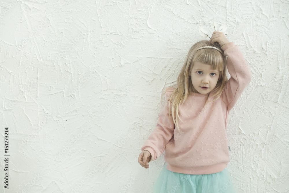Fototapeta premium Little princess girl making fun faces on the white brick wall backgtound