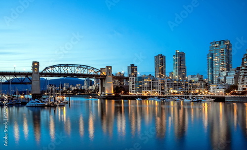 Reflections of city lights in the mirror water of the bay at sunset. Burrard Bridge, Downtown of Vancouver City, British Columbia Canada.