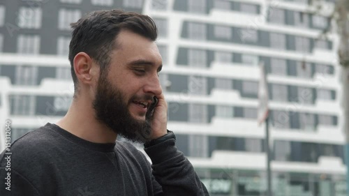 young man with beard talking on the phone near high-rises photo