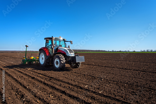 Agriculture tractor sowing seeds and cultivating field. Blue sky 