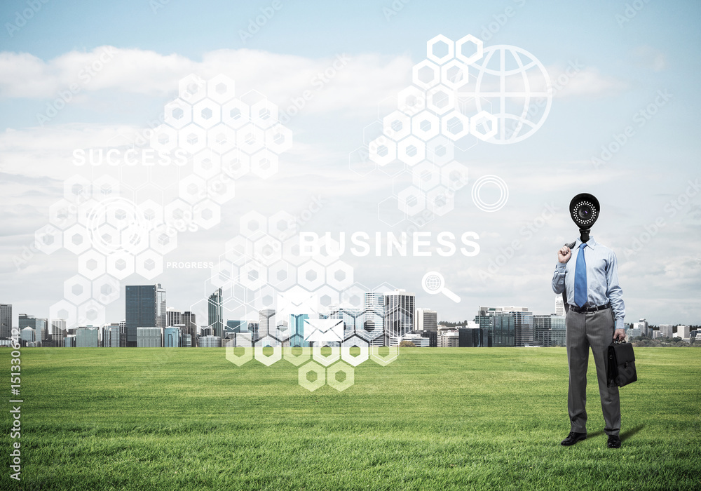 Camera headed man standing on green grass against modern citysca