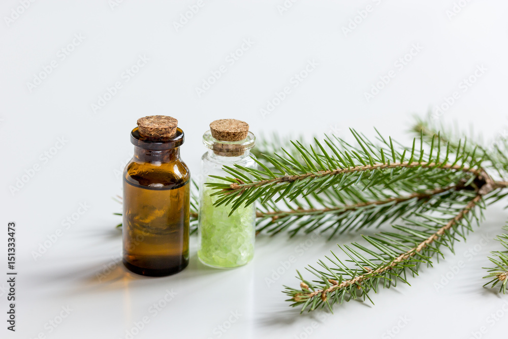 Spruce needle aromatherapy essential oils and salt in bottles on white table background Spruce needle aromatherapy essential oils and salt in bottles on white table background