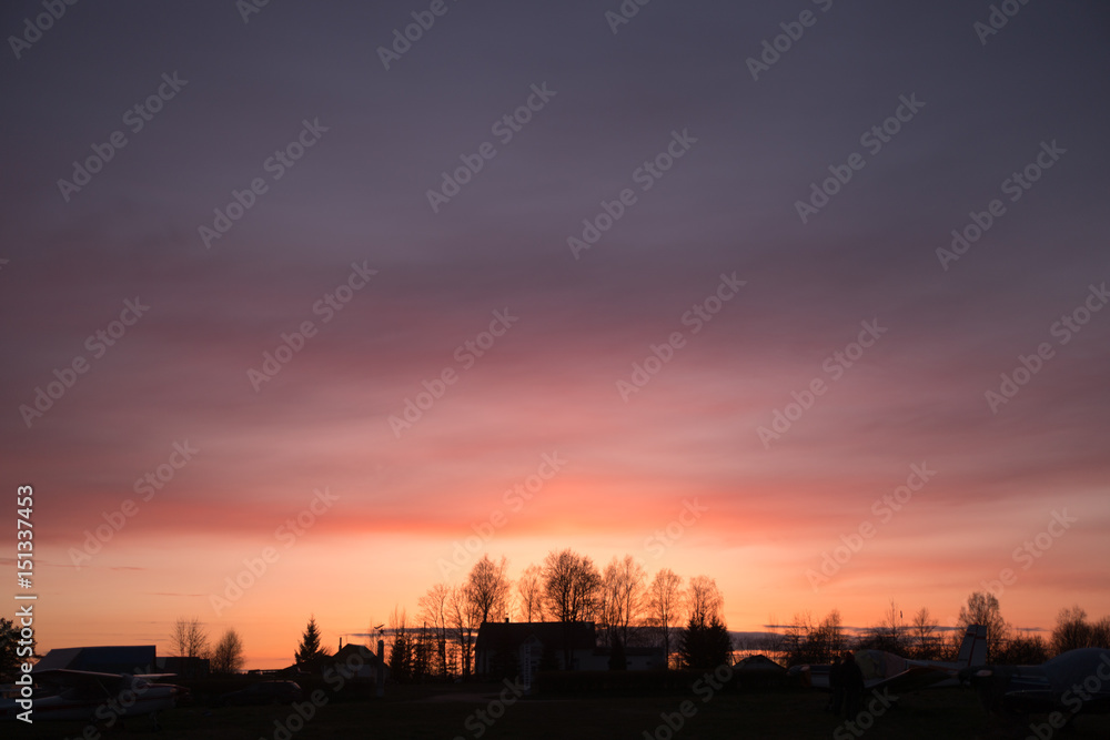 Beautiful sunset at the airfield with blurred clouds and silhouettes of trees and buildings