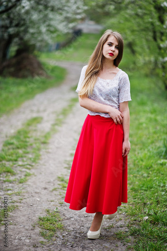 Portrait of beautiful girl with red lips at spring blossom garden, wear on red dress and white blouse. © AS Photo Family
