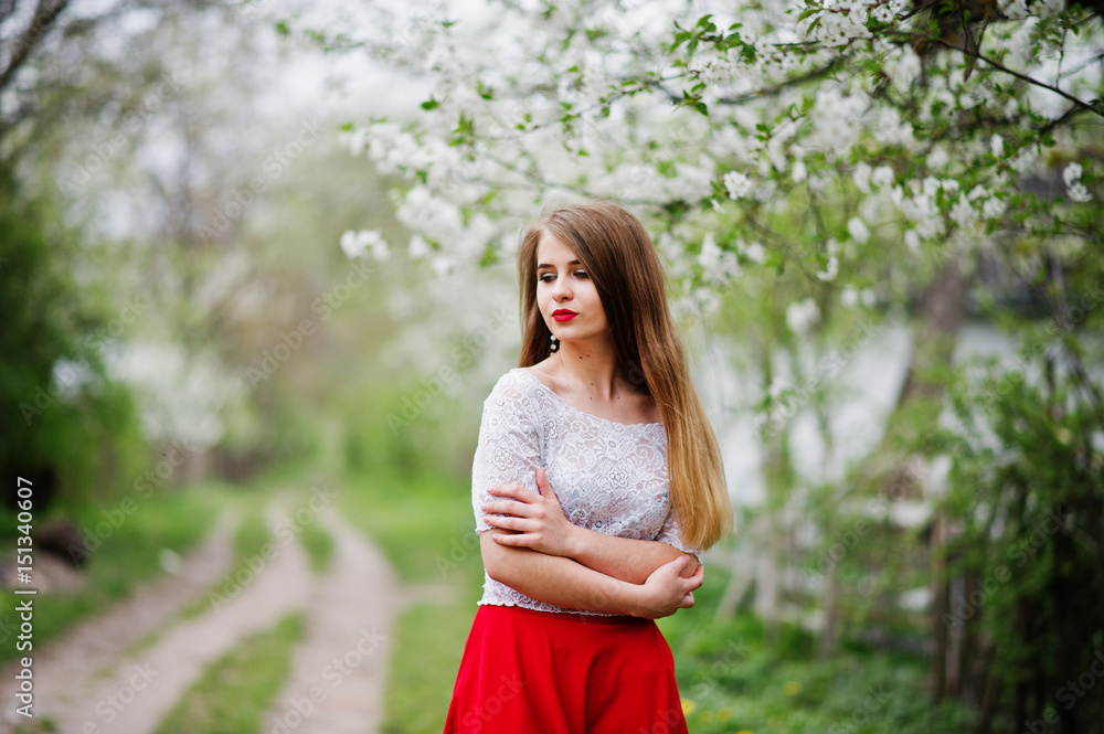 Portrait of beautiful girl with red lips at spring blossom garden, wear on red dress and white blouse.