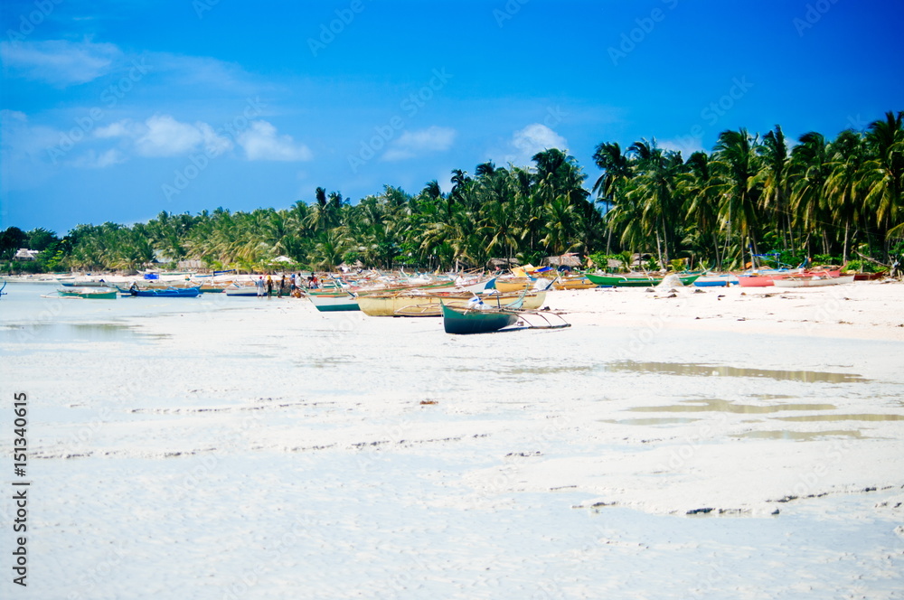 Tropical white sand beach with green palm trees and parked fishing boats in the sand. Exotic island paradise
