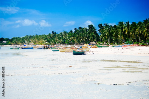 Fototapeta Naklejka Na Ścianę i Meble -  Tropical white sand beach with green palm trees and parked fishing boats in the sand. Exotic island paradise
