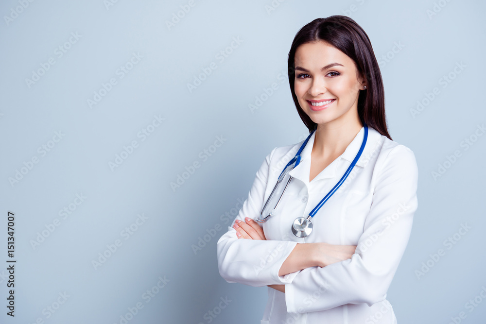 Portrait of glad smiling doctor in white uniform standing with crossed hands on gray background Portrait of glad smiling doctor in white uniform standing with crossed hands on gray background