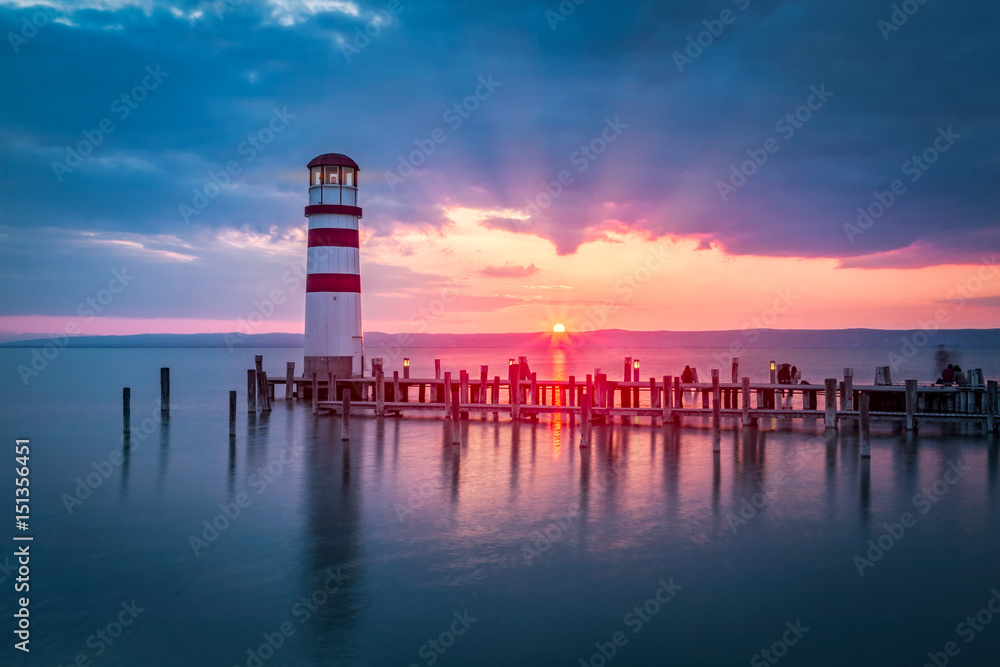 Lakeside sunset scenery with lighthouse on a peer
