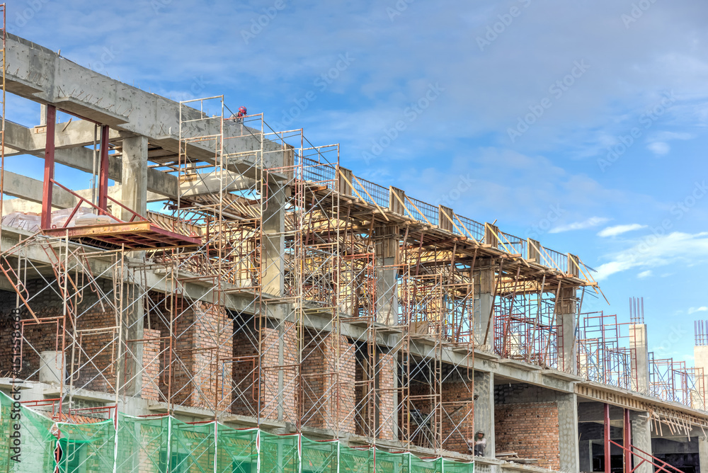 Office and residential building under construction and blue sky. Safety net, green grid prevent object falling from height in Malacca, Malaysia. Scaffolding, formwork in installation, building fencing Office and residential building under construction and blue sky. Safety net, green grid prevent object falling from height in Malacca, Malaysia. Scaffolding, formwork in installation, building fencing