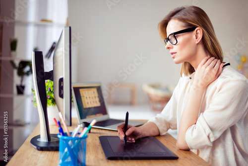 Concentrated young woman in glasses retouching photo for a long time and having pain in her neck